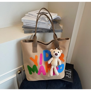 Detail of khaki canvas tote bag with colorful letters and cute white teddy bear charm