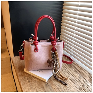 Detail of pink suede bucket bag with red round handle and decorative charms