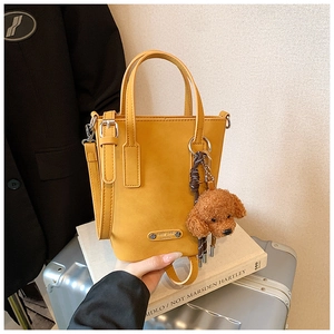 Detail of dark yellow leather bucket bag with metal logo and brown teddy dog charm