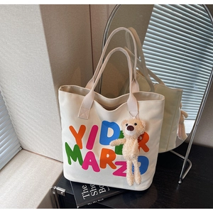 Detailed shot of beige canvas tote bag with letter print and plush bear accessory