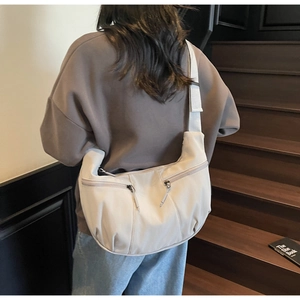 Détail d'un sac bandoulière beige en forme de croissant avec doubles poches zippées