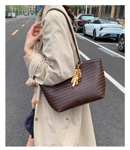 Détail d'un sac cabas tressé marron foncé avec pendentif à perles colorées