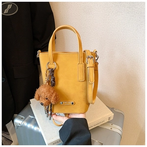 Close-up of a yellow mini crossbody bag with a plush bear charm on white books