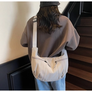 Rear view of a model wearing a beige nylon crescent crossbody bag on a wooden staircase