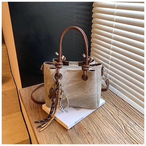 Detail of a beige bucket bag with brown leather handles and a heart fringe charm