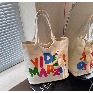 Detail of canvas tote bag with colorful letters and a cute plush bear pendant