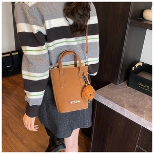 Brown faux leather bucket bag with top handles, crossbody strap, and bear keychain charm