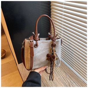 Detail of vintage beige bucket bag with brown leather handles and decorative bow pendant
