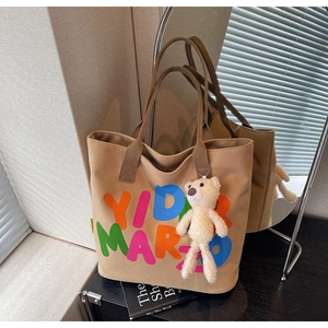 Detail of khaki canvas tote with gradient typography and a cream plush bear charm