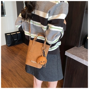 Classic brown leather tote bag detail with cute teddy bear charm and adjustable shoulder strap