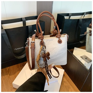 Detail of canvas bucket bag with brown leather handles and a decorative heart bow charm