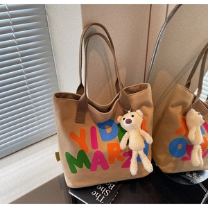 Detail of khaki canvas tote bag with artistic letter print and cute plush bear charm