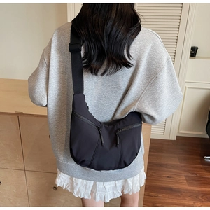 Gros plan du sac bandoulière noir en nylon avec deux poches zippées diagonales sur le devant