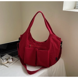Detail of red nylon tote bag with multi-pocket design and reinforced woven shoulder strap