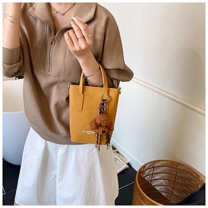 Close-up of yellow PU leather crossbody bag featuring a cute brown teddy bear keychain