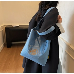 Detail of light blue denim tote bag with orange embroidered today mood text on pocket