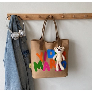 Detail of khaki canvas tote bag with letter print and cute white plush bear charm