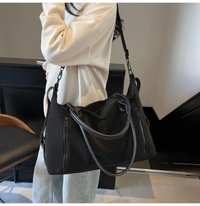 Detail of a large black travel tote with leather handles and textured nylon fabric on a model