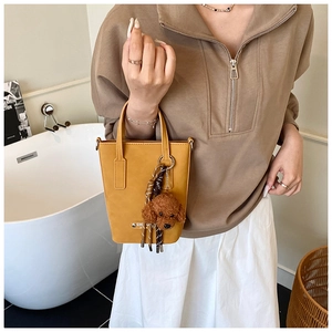 Detailed view of yellow leather tote bag featuring a cute brown plush dog charm