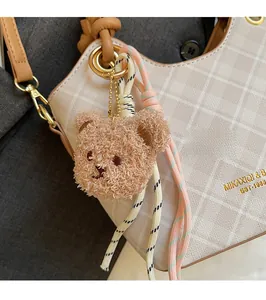 Dettaglio di un orsetto di peluche marrone con corde intrecciate su una borsa beige trapuntata