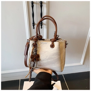Detailed shot of cream retro bucket bag with brown handles and a bow pendant