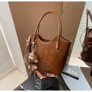 Brown leather tote bag featuring unique wavy cut edges and a plush monster charm