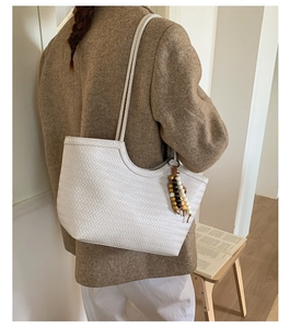 Détail du sac cabas tressé blanc avec texture en cuir et breloque en perles de bois
