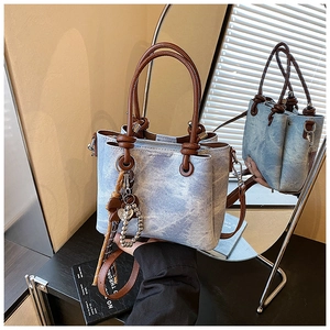 Detail of blue denim bucket bag featuring brown leather straps and heart charm with pearls