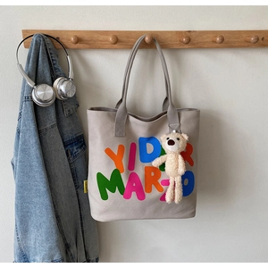Detail of canvas tote bag with colorful YIID MARIO lettering and a plush bear charm