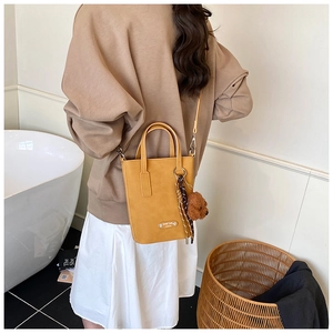 Detail of yellow crossbody bag with cute plush bear and silk scarf on a sleek leather finish
