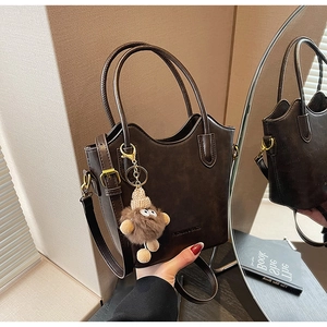Detailed view of dark brown tote bag with embossed letters and a cute plush bear charm