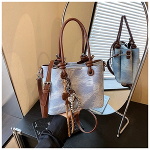 Detailed side view of blue denim tote bag with leather handles and decorative floral charms