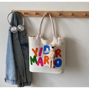 Detail of cream canvas tote bag with bold lettering and a cute brown plush bear charm