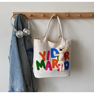 Detailed shot of a white canvas tote bag with colorful letters and plush bear charm