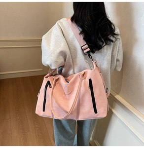 Detail of light pink travel bag showing matte texture, black zippers, and wide shoulder strap