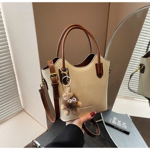 Detail of cream crossbody bucket bag with brown handles and a cute plush monster charm