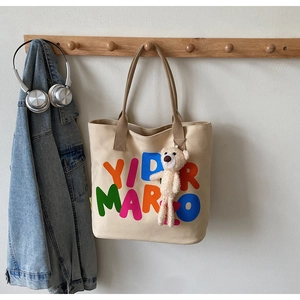Detail view of canvas tote bag with colorful letters and cute teddy bear pendant