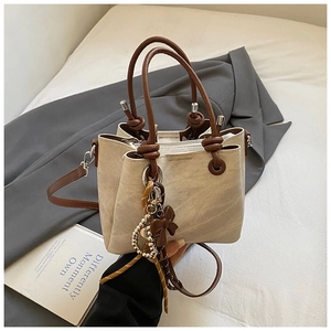 Detail of a beige bucket bag with brown handles and a decorative bow charm on a bed