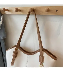 Detail of adjustable shoulder strap with gold buckle on a white and brown tote bag
