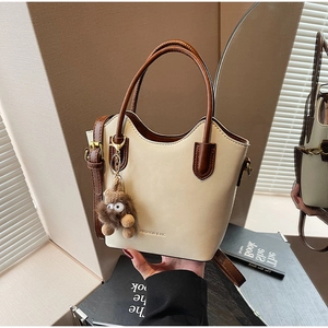Detail of a cream and brown bucket bag with wave-edge trim and a cute plush charm