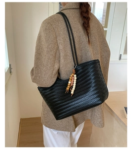 Détail d'un sac cabas tissé noir avec pendentif en perles de bois sur la bandoulière