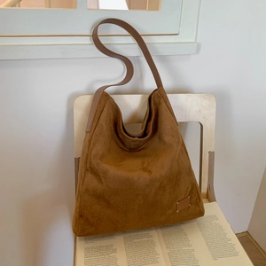 Brown vintage hobo tote bag in matte suede texture placed on a wooden chair with books