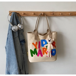 Close-up of beige canvas tote bag with YID MARIO lettering and plush bear charm
