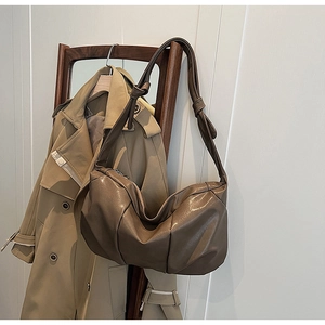 Detail of coffee brown ruched shoulder bag with knotted strap on a wooden frame