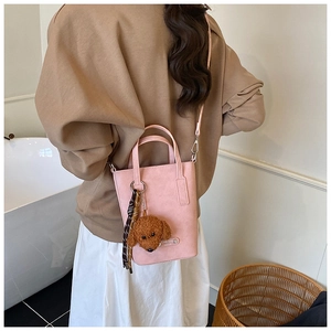 Pink crossbody bag with a teddy bear charm and pattern strap shown in a minimal scene