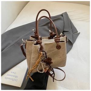 Close-up of beige bucket bag with brown handles and elegant bow ornaments on grey blazer