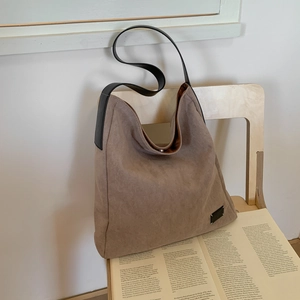 Detail of matte khaki tote bag with black leather strap on a wooden chair