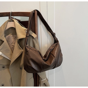 Detail of a brown pleated crescent bag with knot strap on a wooden hanger