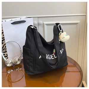 Large black canvas tote bag with white ANGEL logo and cute plush charm on a table