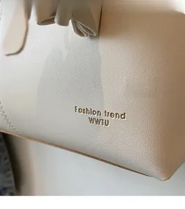 Detail of white leather tote bag featuring gold foil fashion text and delicate bow accent